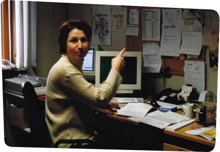 Mitarbeiterin im Büro Mitarbeiterin sitzt an Arbeitsplat mit Computer und zeigt mit dem Finger auf die Infotafel an der Wand