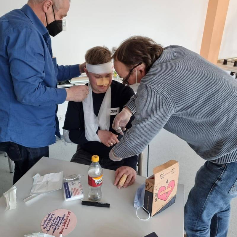2 Ersthelfer legen einem Mann Verbände an