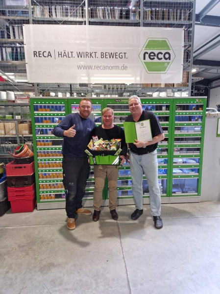 2 Geschäftsführer mit einem Partner, der eine Auszeichnung und einen Geschenkkorb erhält