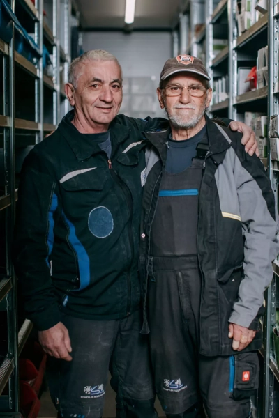 Teamfoto: 2 Mitarbeiter der Firma. Ein Mitarbeiter legt den Arm auf die Schulter des Kollegen