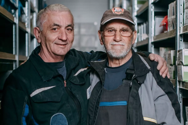 Teamfoto: 2 Mitarbeiter der Firma. Ein Mitarbeiter legt den Arm auf die Schulter des Kollegen