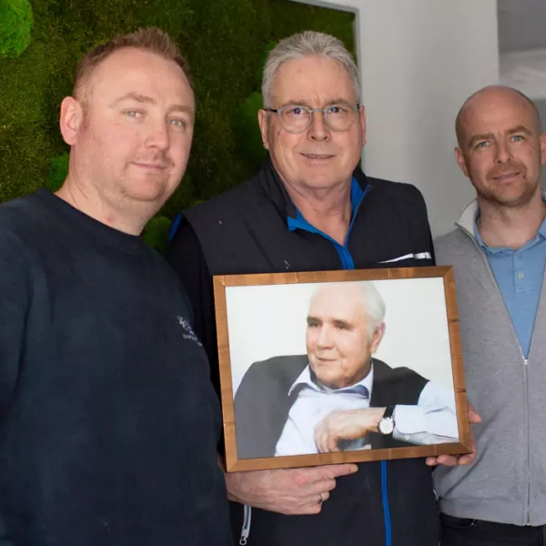 Foto der 3 Geschäftsführer: v.l.n.r. Benjamin Schuppler, Martin Schuppler, Sebastian Schuppler. Martin Schuppler hält ein Foto des Firmengründers